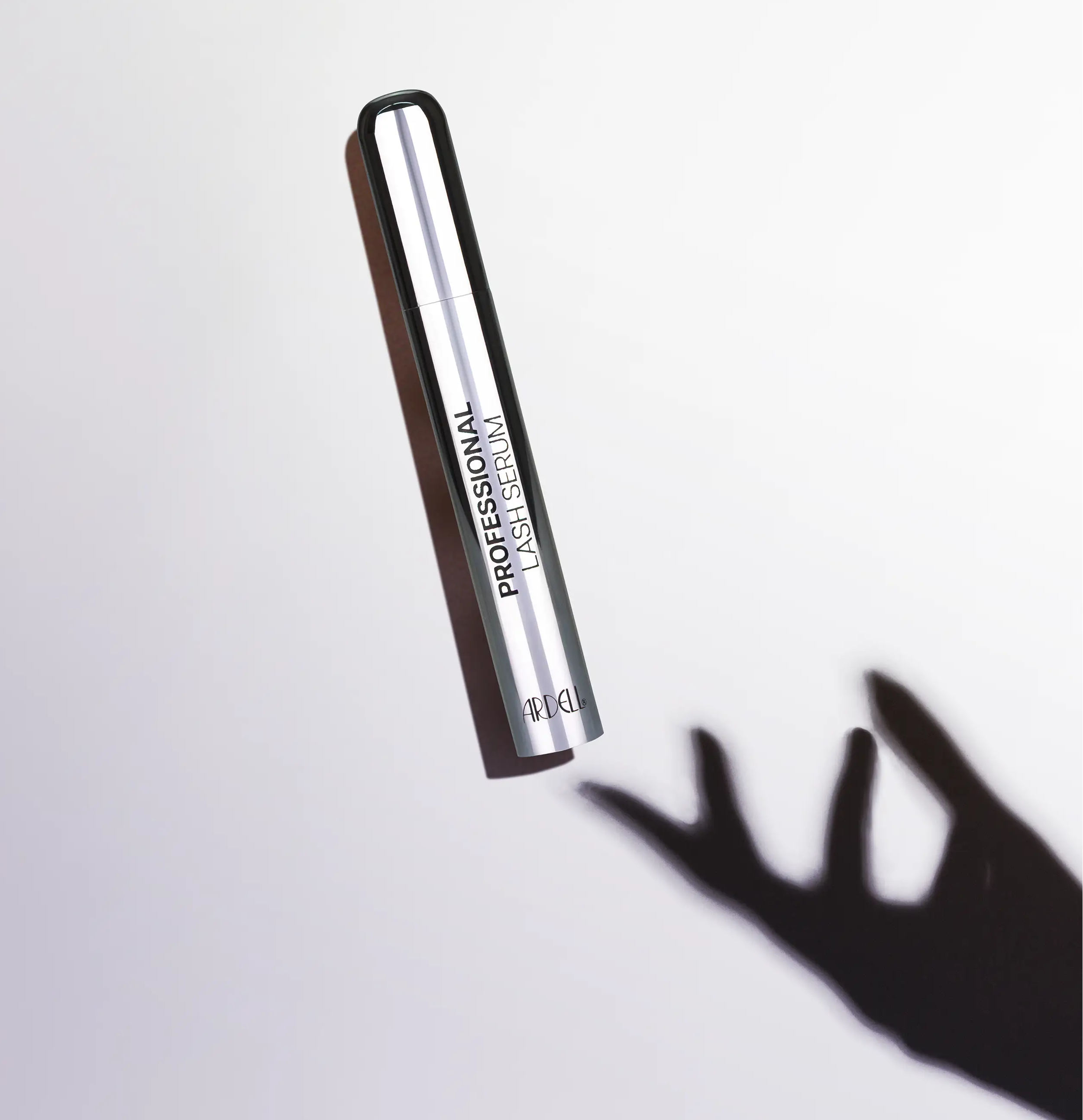 Silberner Flacon des Professional Lash Serum liegt am Boden und ein Schatten einer Hand greift danach.