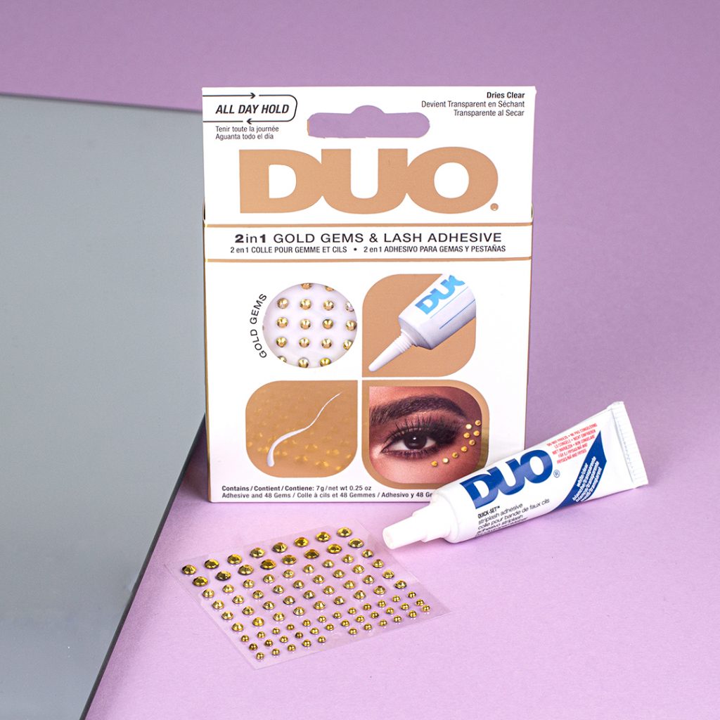 DUO 2 in 1 Gold Gems & Lash Adhesive sind vor einem lilanen Hintergrund zu sehen. 