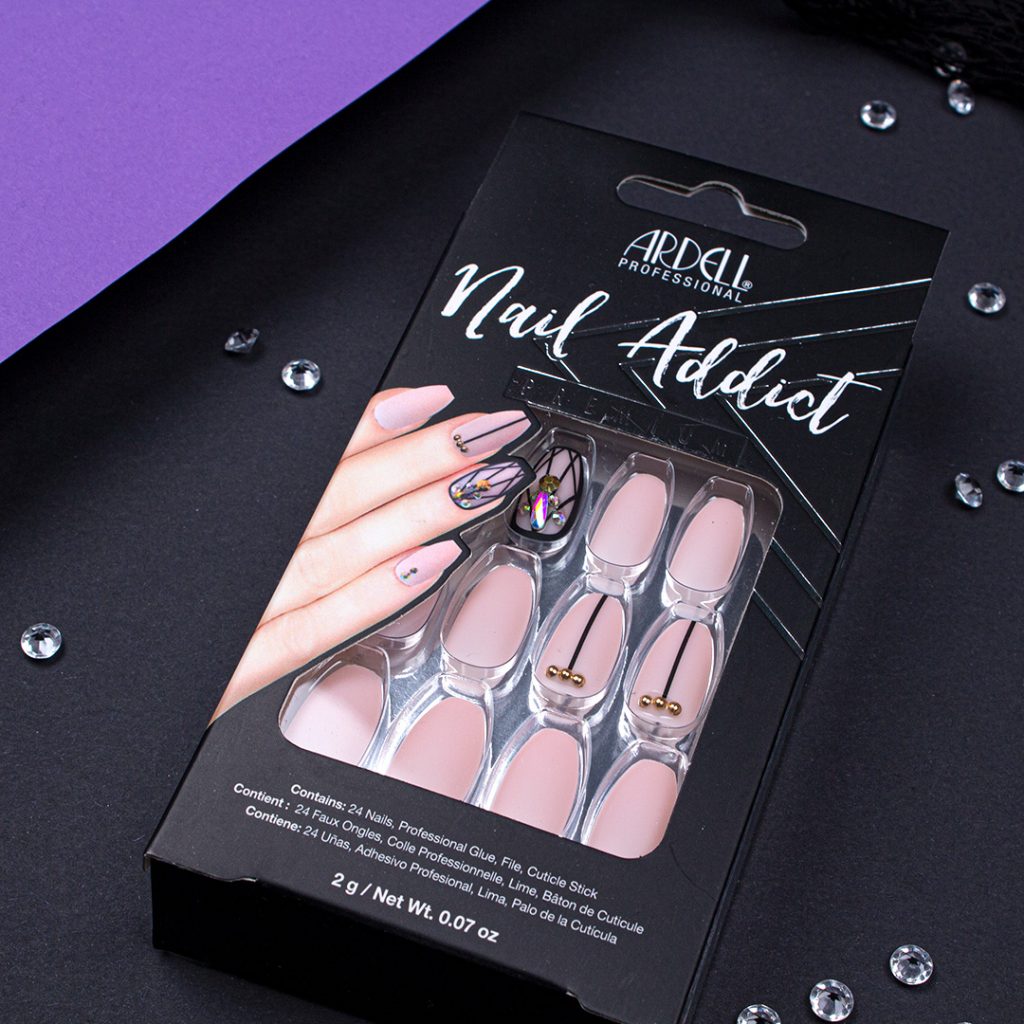Auf schwarzem Hintergrund liegen Nail Addict Blush Geometric Nails. Sie vervollständigen den Halloween Look. Passend zu dem Aussehen der Fake Nails liegen Glitzersteinchen drumherum.