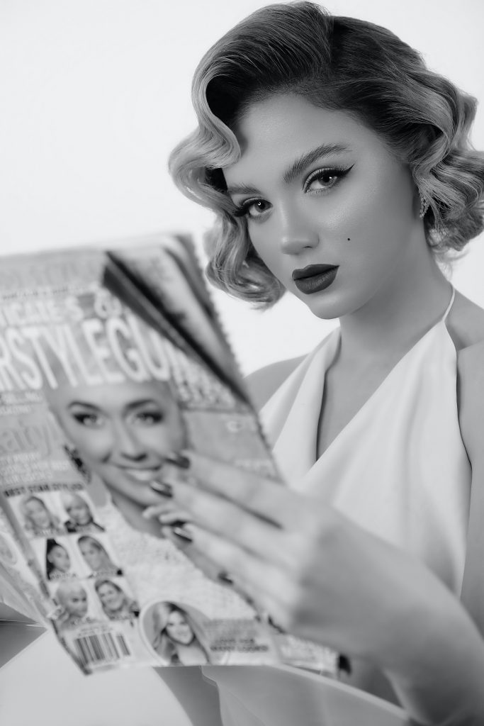 Eine Frau trägt ein Marilyn Monroe Kostüm, in Schwarz/Weiß. Sie hält eine Zeitschrift in der Hand.